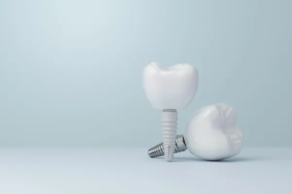 Two dental implant crowns on a pale blue background, showing the precision craftsmanship of the final restoration.