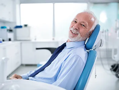 A senior patient smiling in a dental chair during an initial exam in a bright clinic.