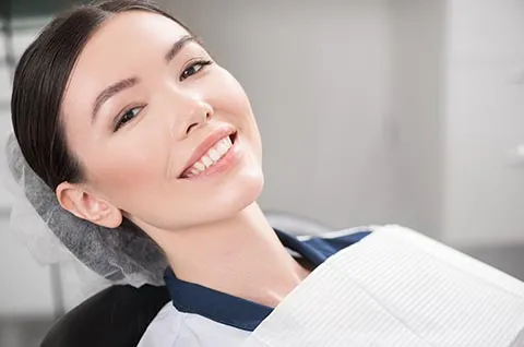 A patient smiles from a dental chair in a bright, modern clinic during a first visit.